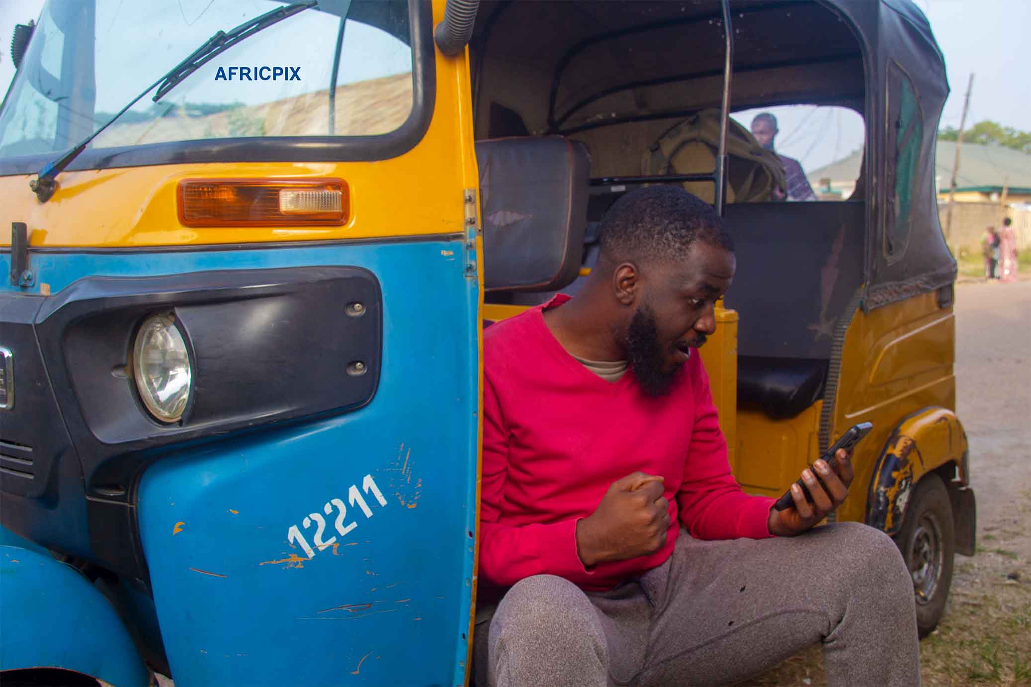 An excited African tricycle rider also known as Keke or Maruwa rider, holding his phone, smiling with joy after receiving good news 4.